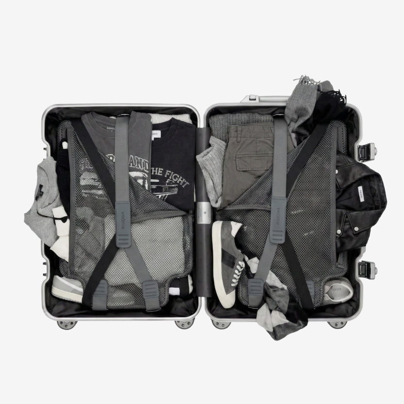 Maleta de mano abierta con ropa y zapatillas desbordándose, mostrando el caos y falta de espacio en el equipaje convencional sin organizadores.